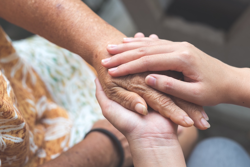 A close up of a senior woman holding hands with a concerned loved one