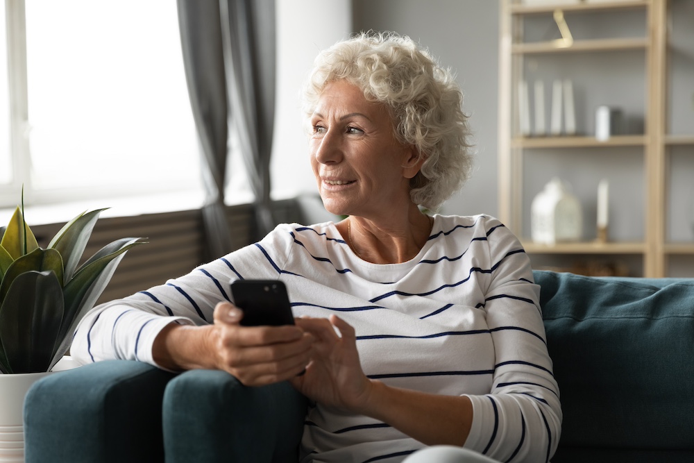 A senior woman using her smart phone while sitting on her sofa