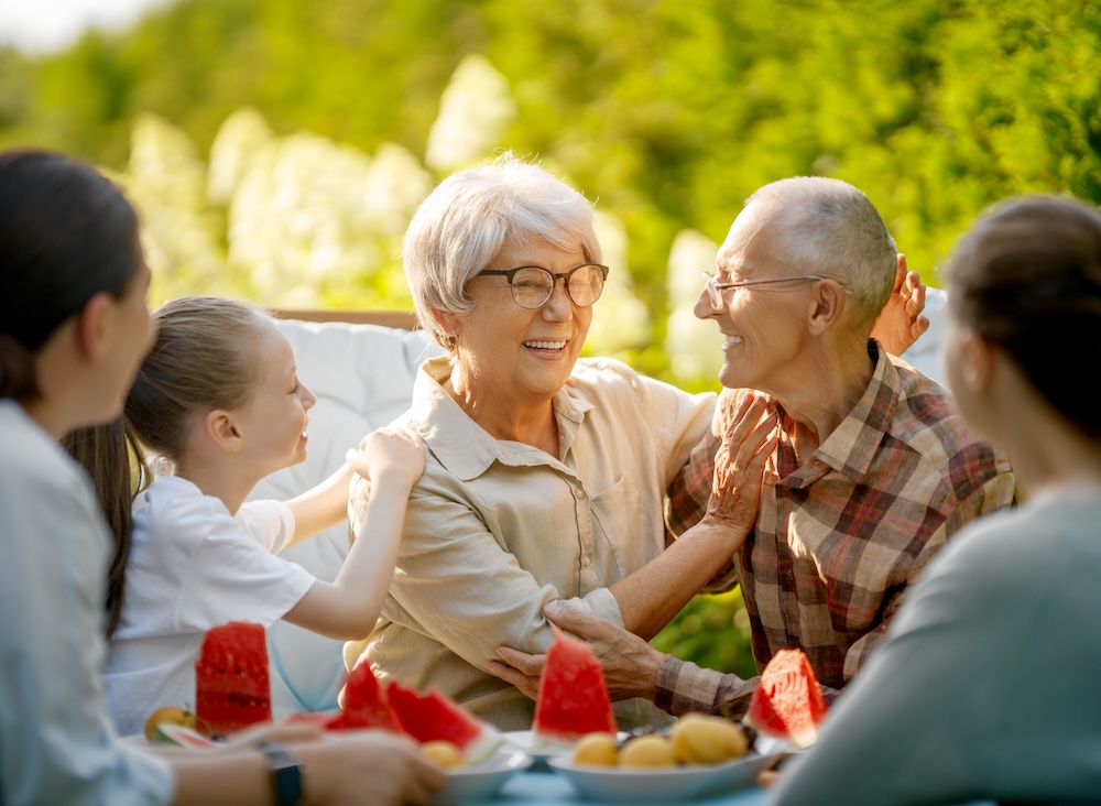 Happy senior couple with young grandchildren outside eating and enjoying the perks of their senior memory care community